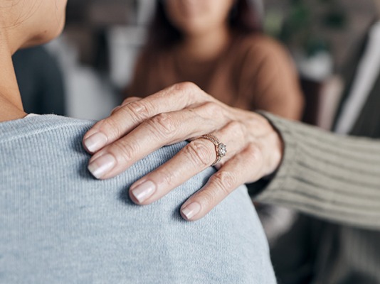 A woman's hand resting supportively on a person's shoulder